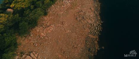 An aerial view of a rocky shoreline with dense greenery and a calm body of water.