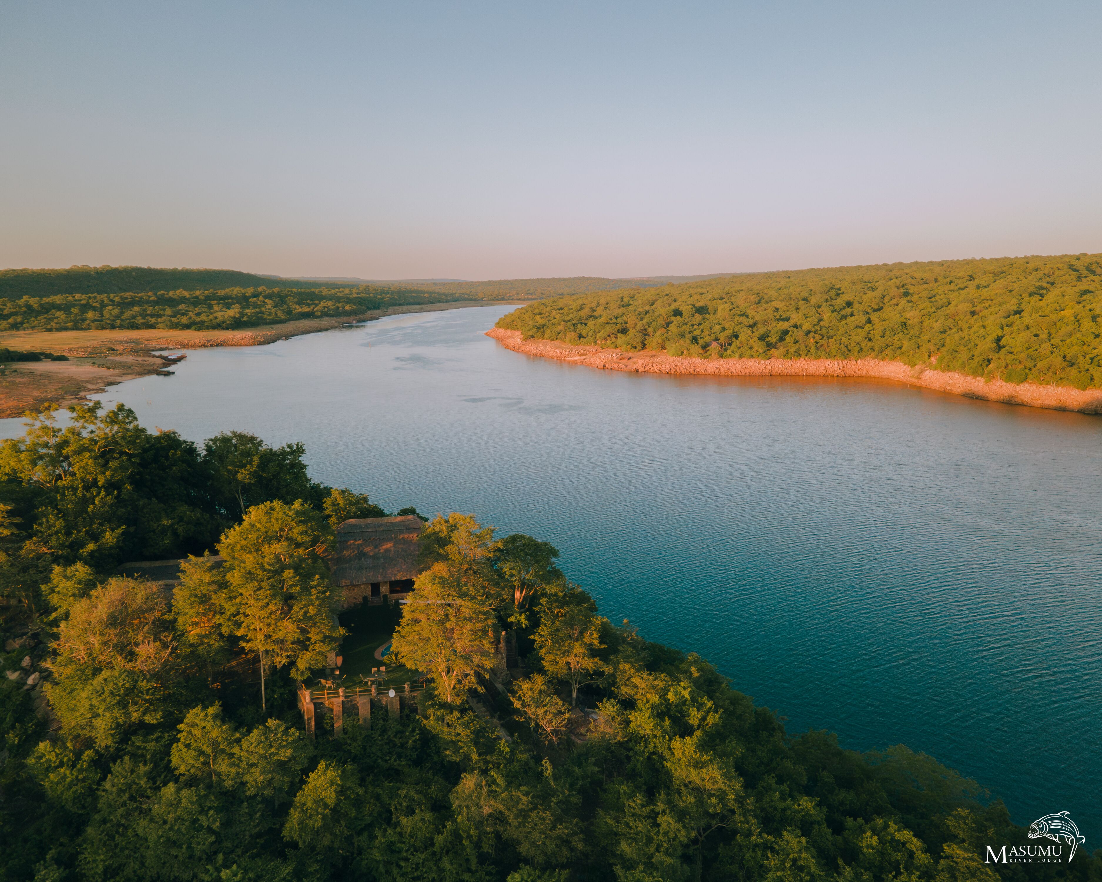 A river surrounded by dense forest, with a small building near the water's edge.