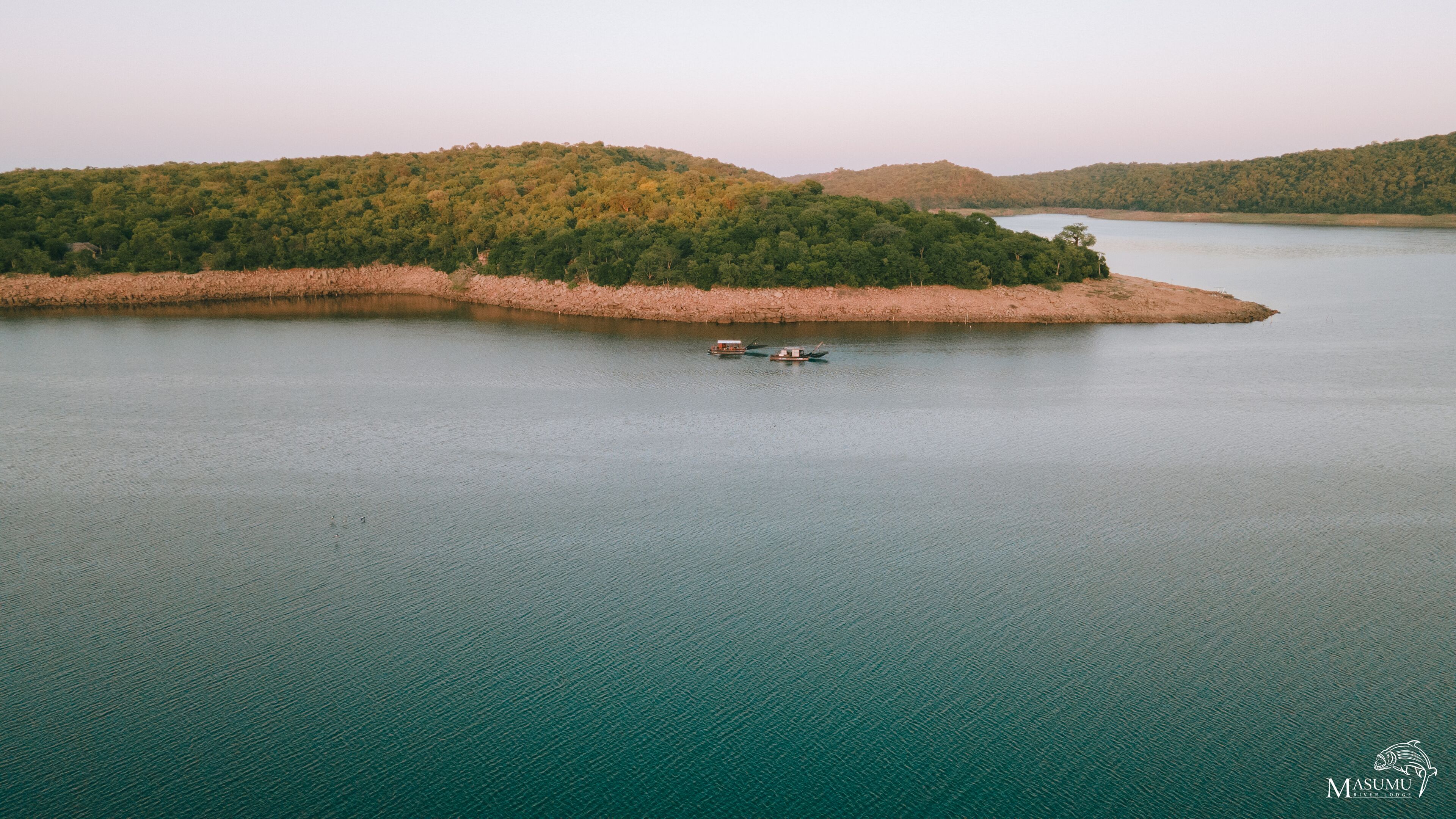 A river surrounded by forested hills with a boat on the water.