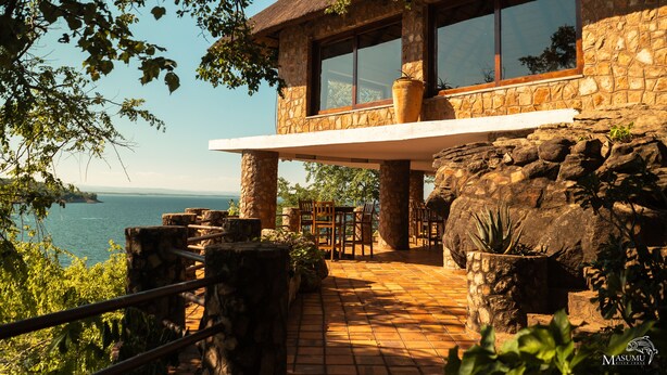 A stone building with a large window and a balcony overlooking a body of water.