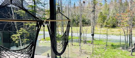Silla hamaca y silla colgante en un espacio exterior cubierto, con vista a un bosque y una carretera.