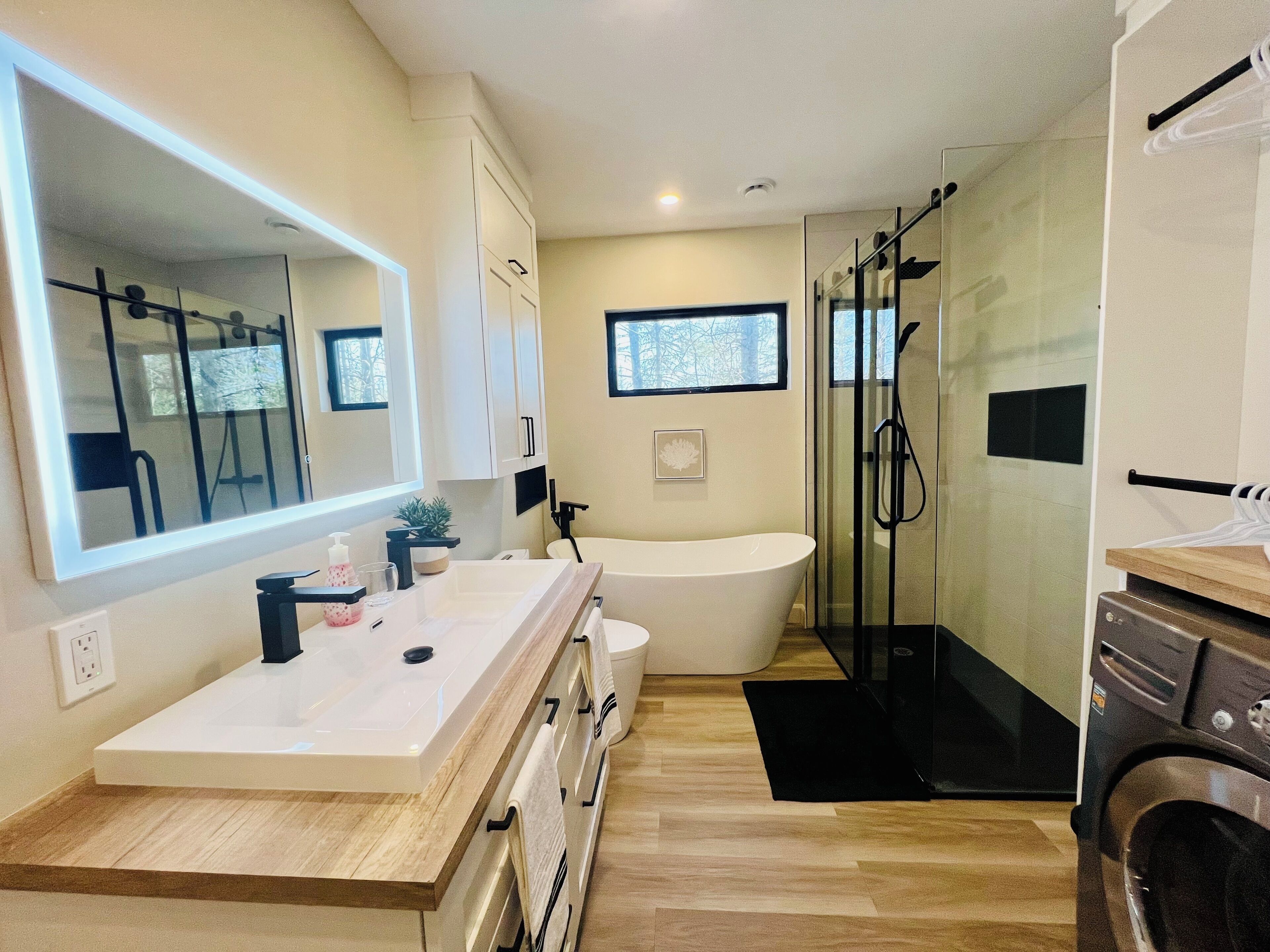 Un bagno moderno con uno specchio grande, una vasca freestanding, una doccia con pareti in vetro e un mobile bagno in legno.