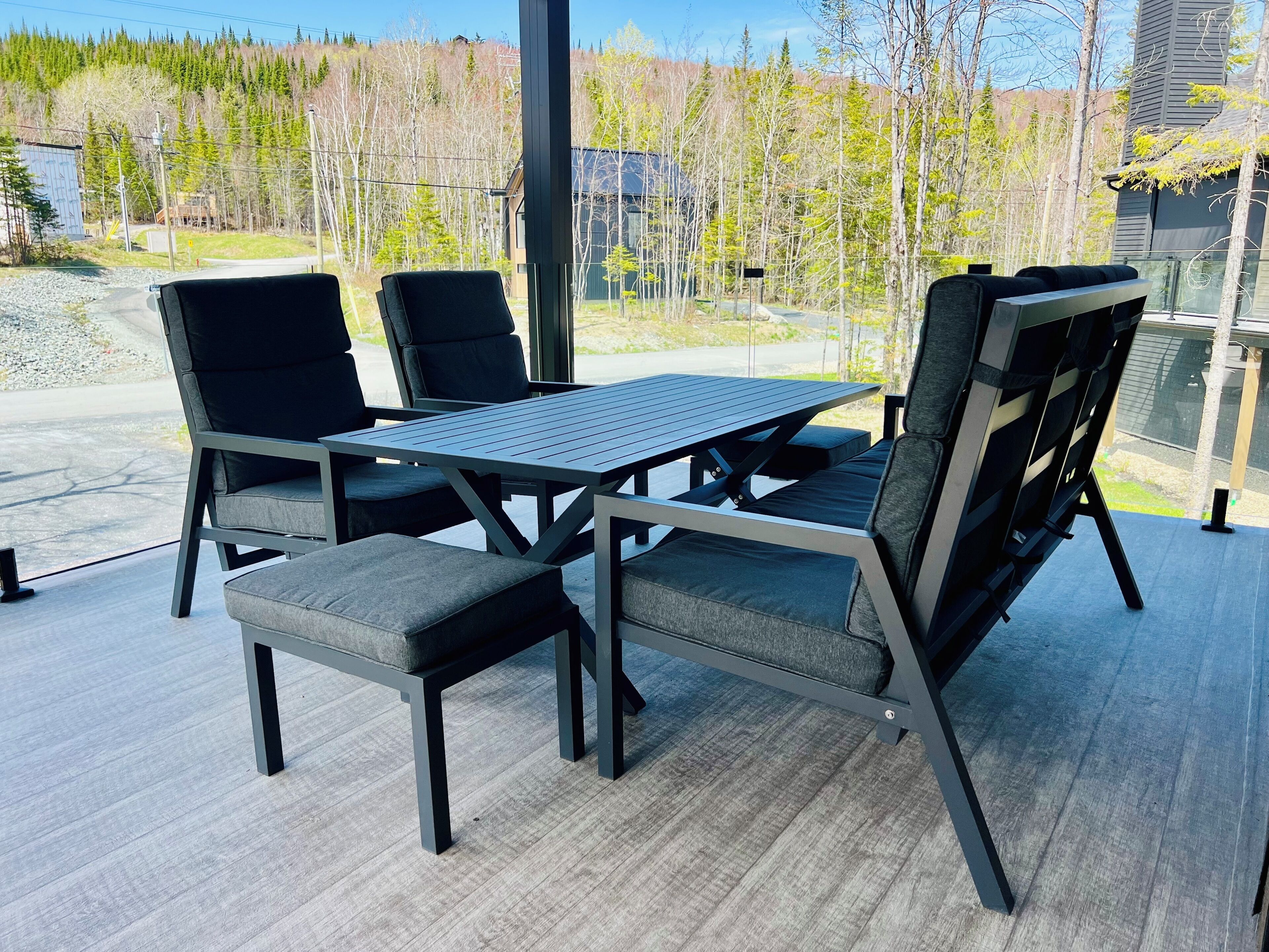 A modern outdoor dining area with a table and chairs, a bench, and a view of a forested area.