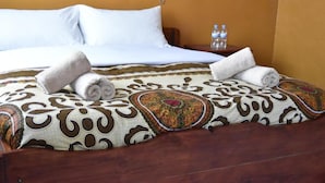A neatly made bed with white linens, a patterned bedspread, and two rolled towels. - Room in B&B - Amahoro Guest House - Queen Room (Muhoza)