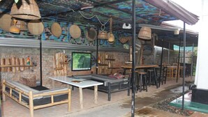 An outdoor seating area with wooden furniture, a television, and decorative baskets. - Room in B&B - Amahoro Guest House - Queen Room (Muhoza)