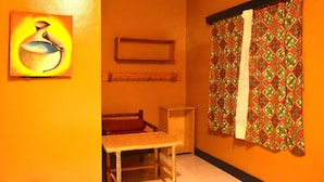 A room with a woven table, a framed artwork, a patterned curtain, and a shelf. - Room in B&B - Amahoro Guest House - Queen Room (Muhoza)