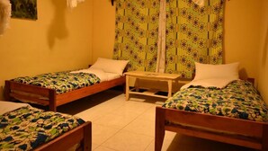 A room with two wooden beds, a small table, and a curtain with a geometric pattern. - Room in B&B - Amahoro Guest House Triple Room With Shared Bathroom (Muhoza)