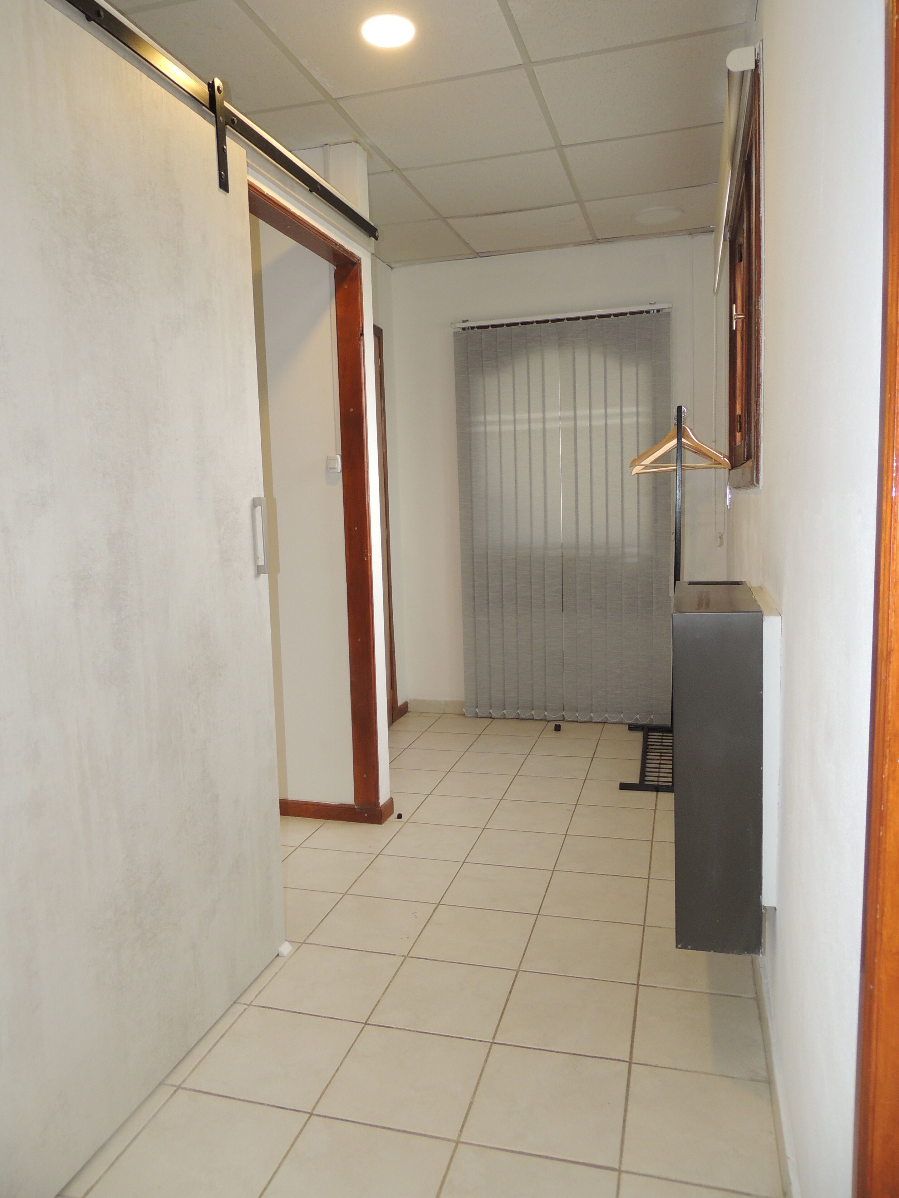 A hallway with a tiled floor, a sliding door, a curtain, and a coat rack.