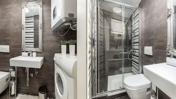 A modern bathroom with a large mirror, a sink, a washing machine, a toilet, and a glass-enclosed shower.