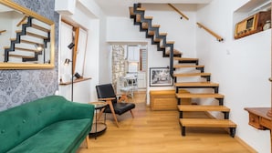Una sala de estar moderna con un sofá verde, una escalera de madera y un comedor con mesa y sillas.