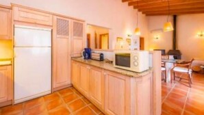 Eine kleine Küche mit Holzausstattung, einem weißen Kühlschrank, einer Mikrowelle und einem Essbereich mit Tisch und Stühlen.