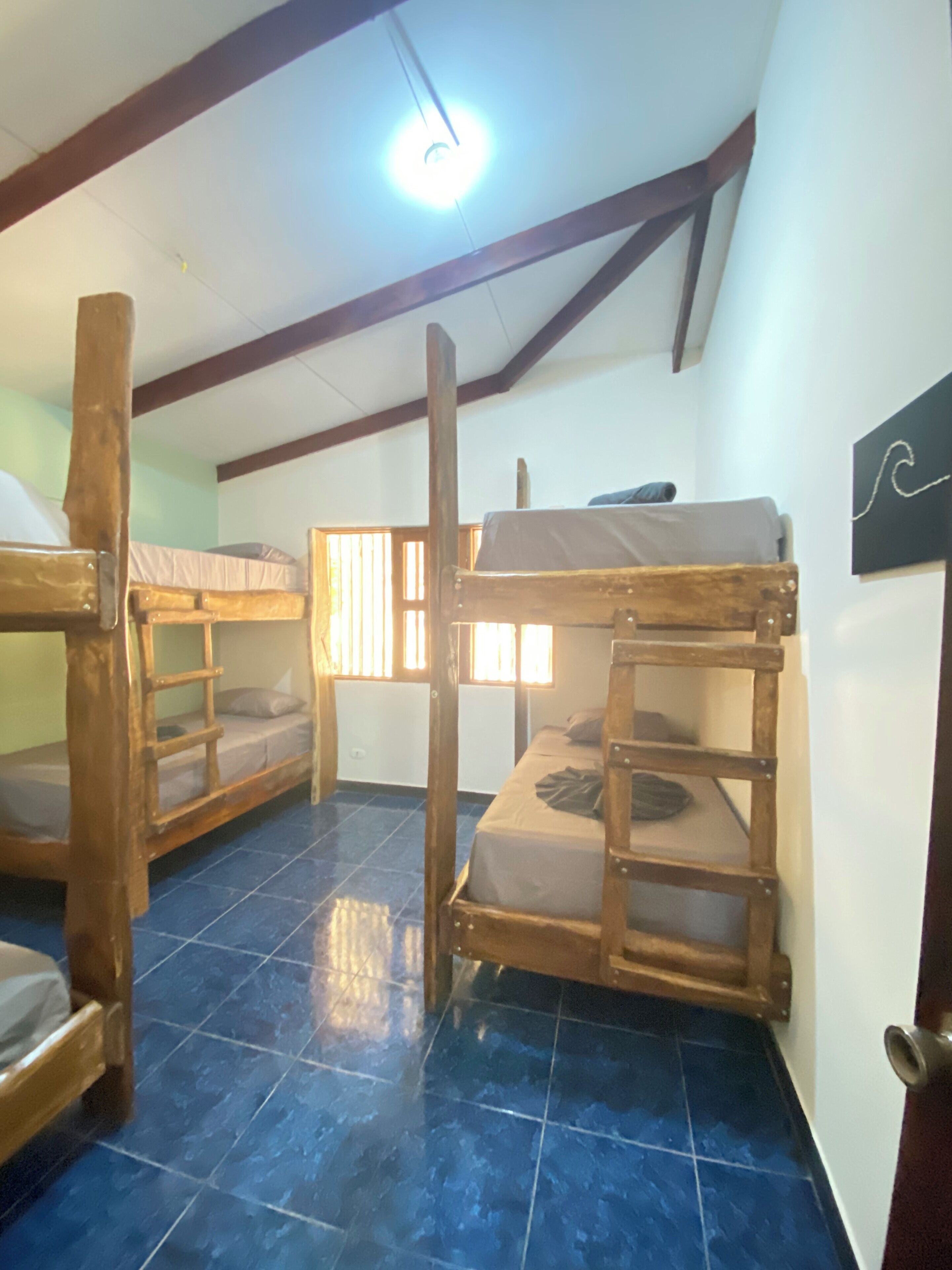 A dormitory room with bunk beds, a tiled floor, and a ceiling light.