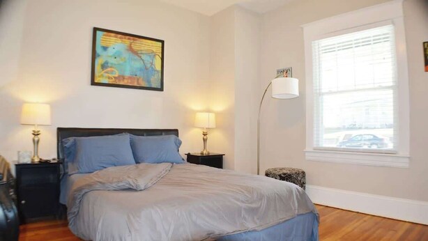 Een slaapkamer met een bed, twee nachtkastjes, een vloerlamp, een raam en een schilderij aan de muur.