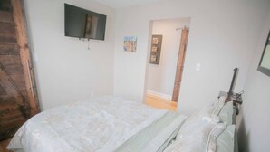 Een slaapkamer met een bed, een aan de muur bevestigde televisie en een deur naar een andere kamer.