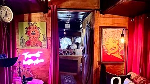 A narrow hallway with a wooden floor, a round table with a pink neon sign, a clock, and a couch with a large number '9' on it. - Spend an evening w Trolley Parton! #Love #IndoorProjector #Vibes #Renew (Doyle)