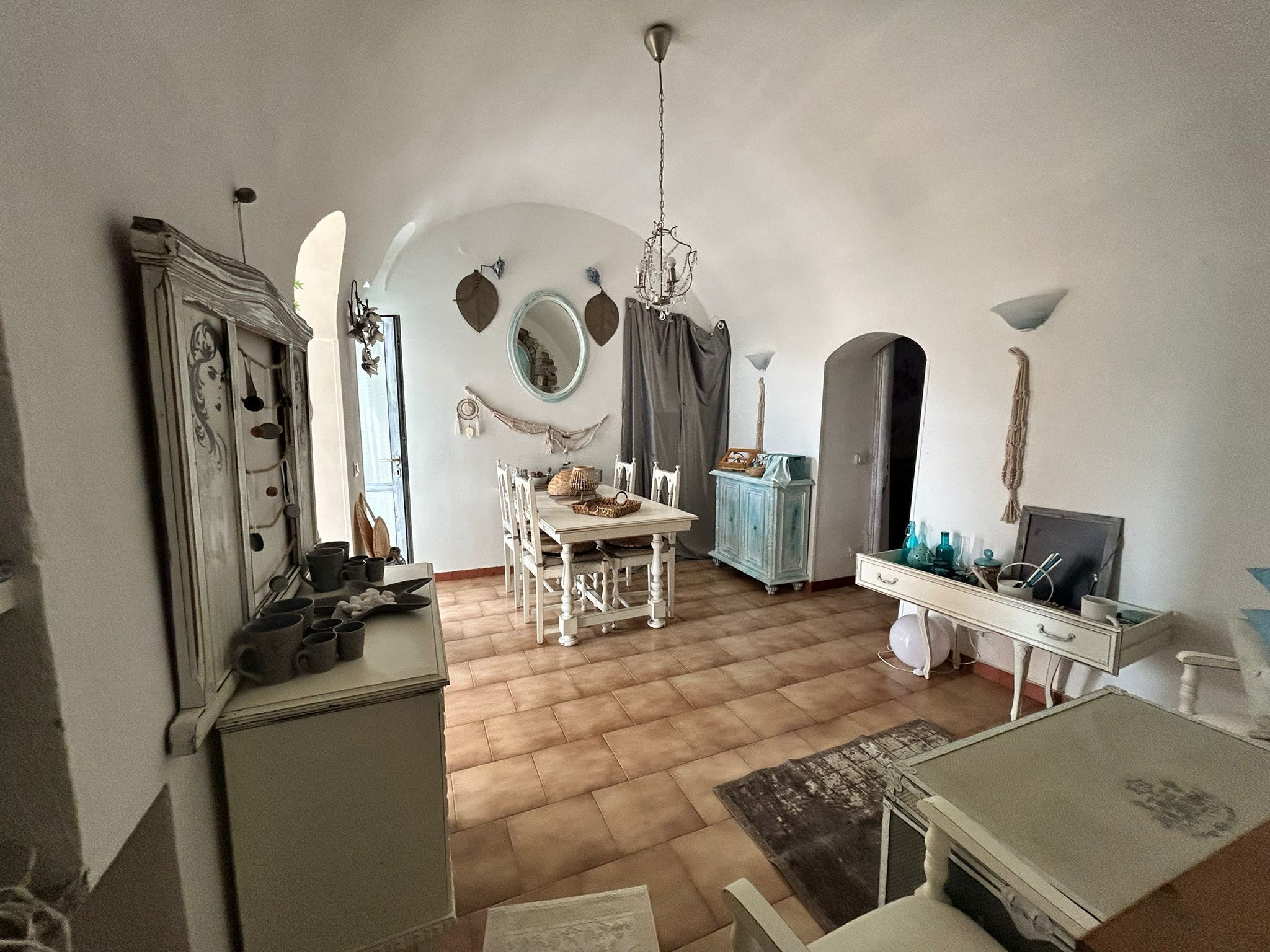 Ein Zimmer mit Esstisch, Stühlen, einer Kristallleuchtre, einem Spiegel und einem Schrank.