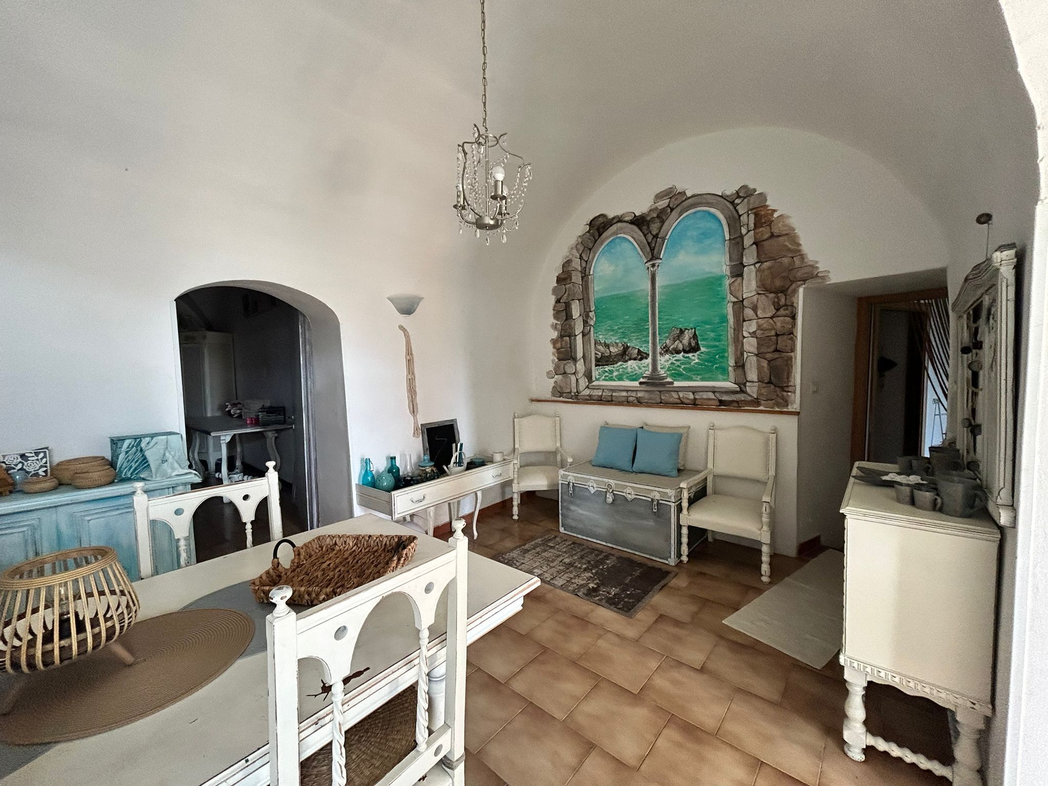 A spacious living room with a stone wall mural, a white sofa, a dining table, and a chandelier.