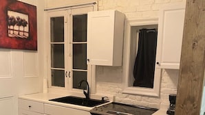 A compact kitchen with white cabinetry, a black stove, and a window with a black curtain.