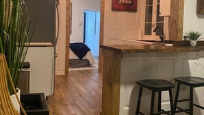 A kitchen with wooden flooring, a refrigerator, a bar counter with stools, and a dining area with a table and chairs.