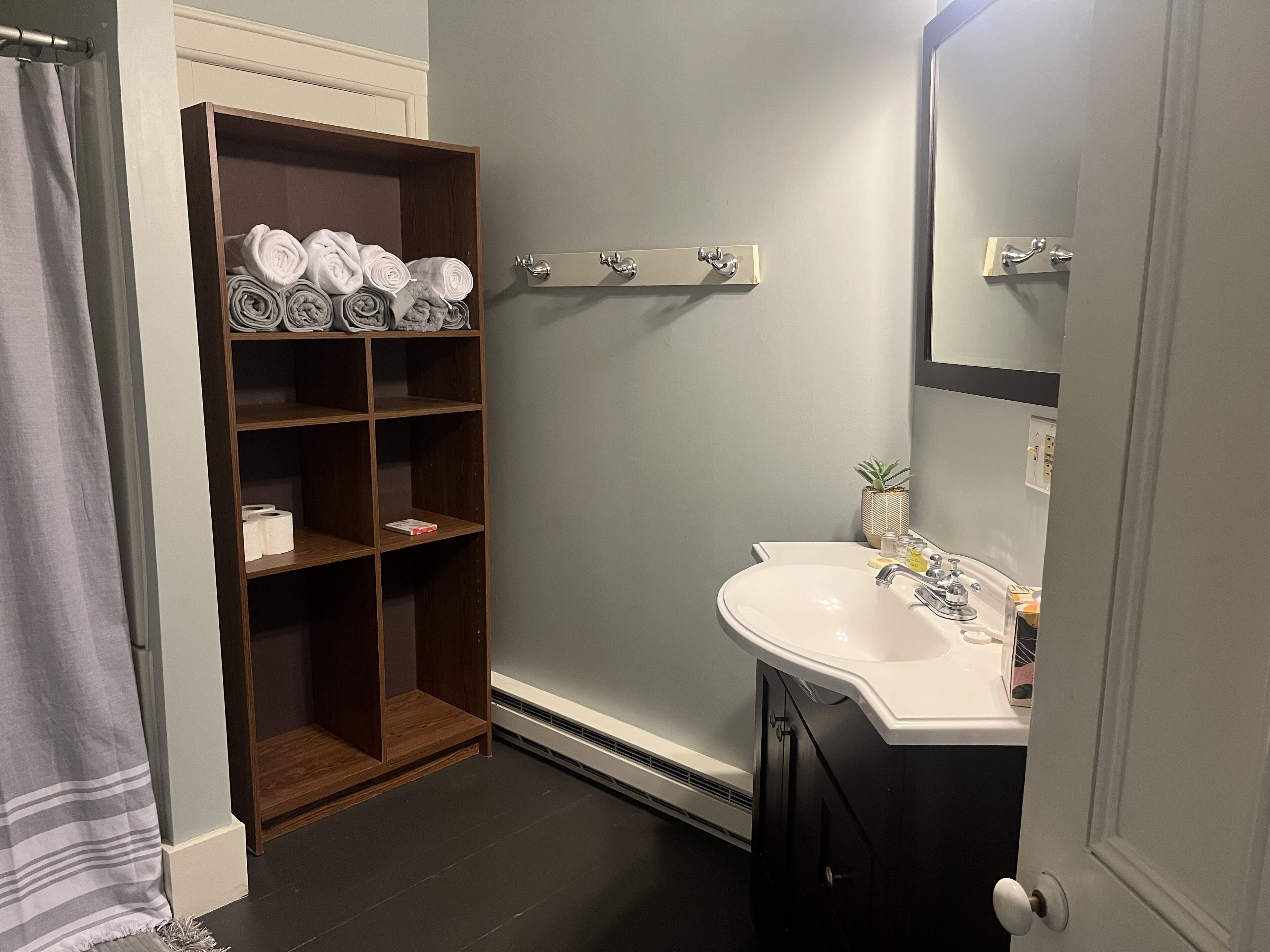 A bathroom with a wooden shelf holding towels, a white sink with toiletries, and a mirror above it.