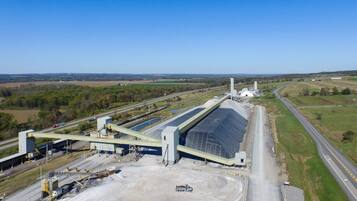 Una instalación industrial con tanques de almacenamiento grandes, cintas transportadoras y una carretera a su lado.