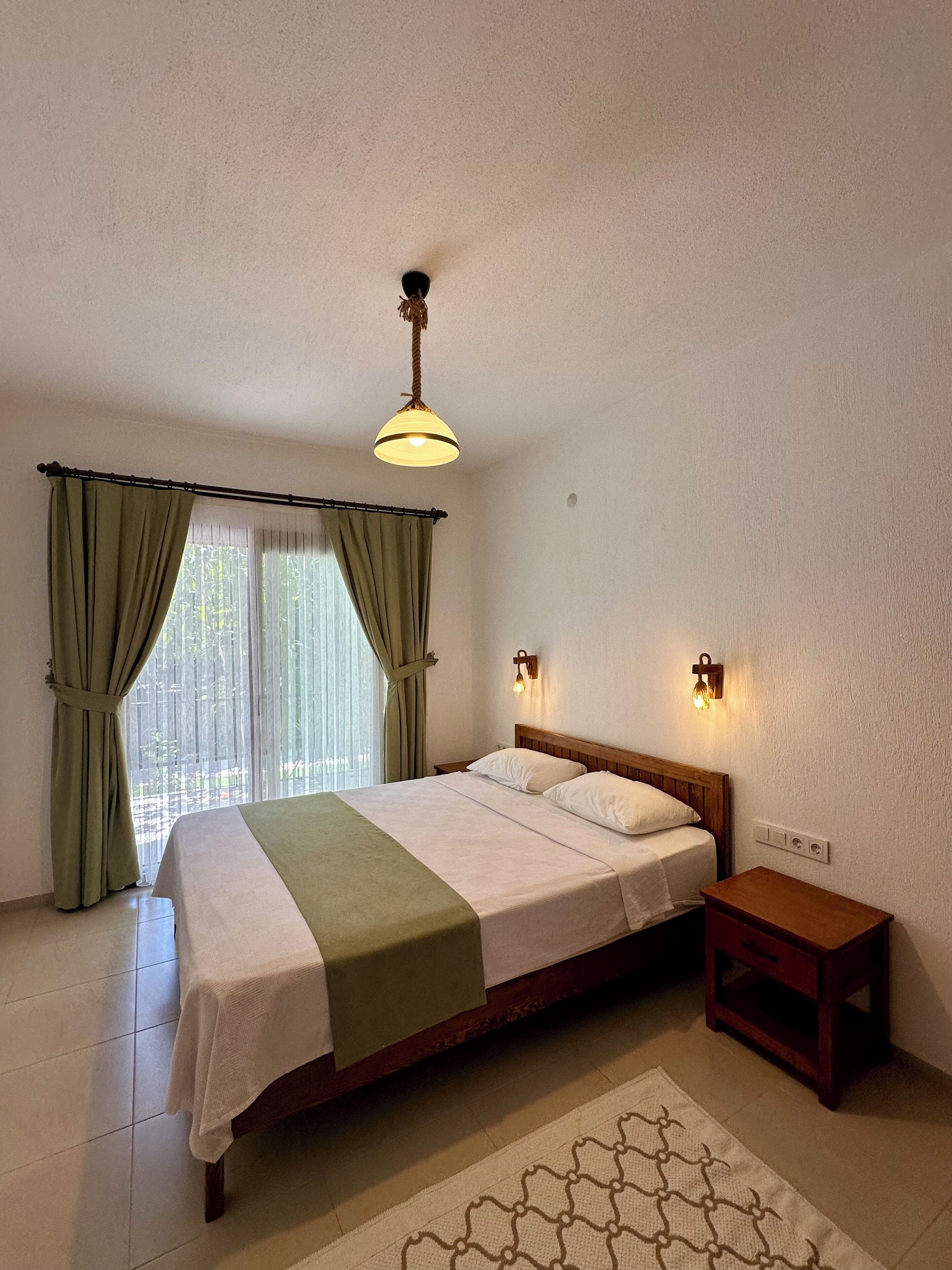A bedroom with a bed, curtains, a bedside table, and a hanging light fixture.