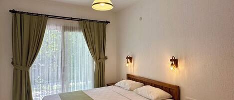 A bedroom with a bed, curtains, a bedside table, and a hanging light fixture.