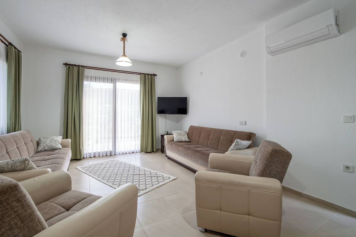 A modern living room with a sofa set, a coffee table, and a flat-screen TV mounted on the wall.