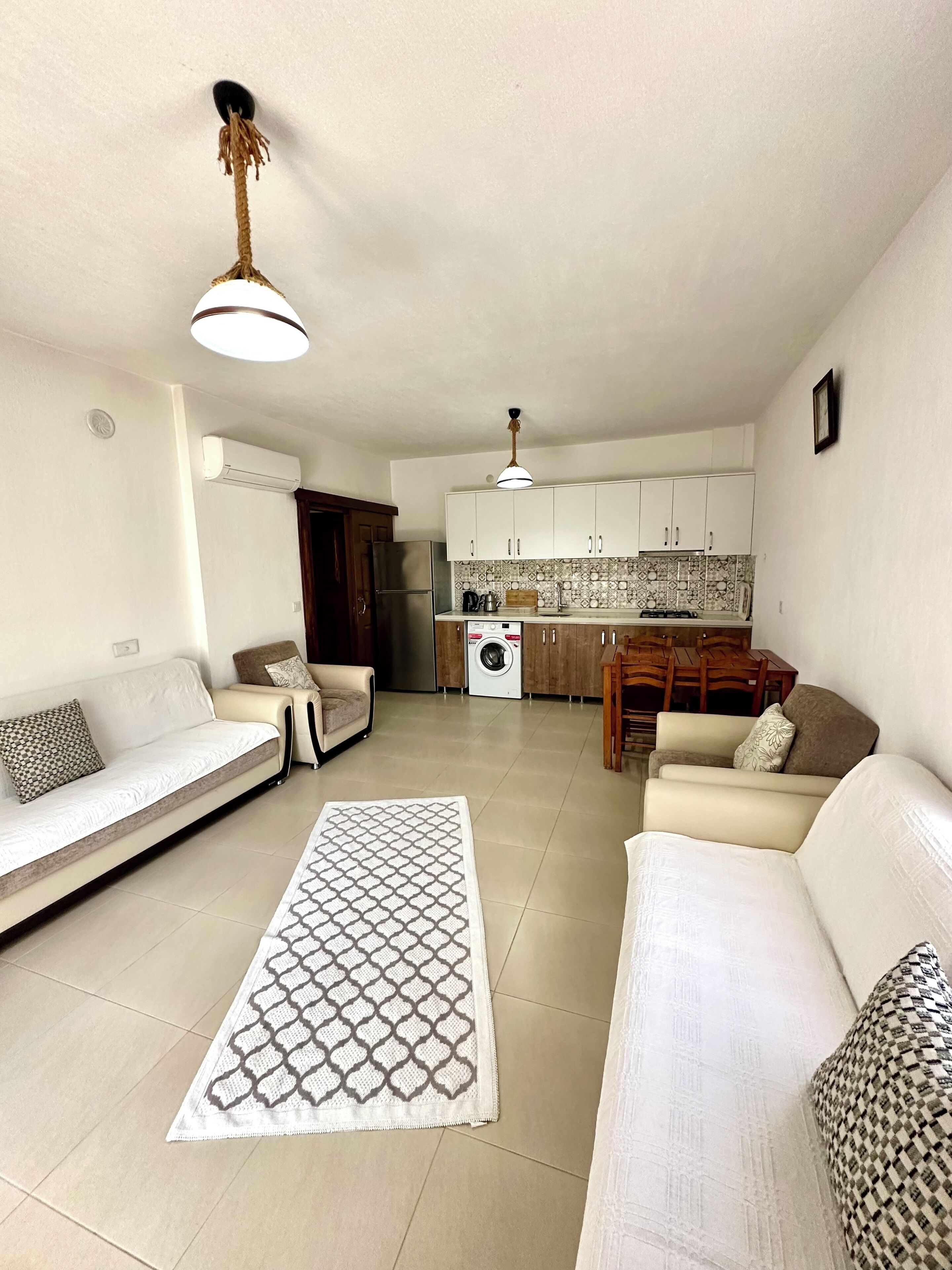 A living room with a sofa, a patterned rug, and a kitchen in the background.