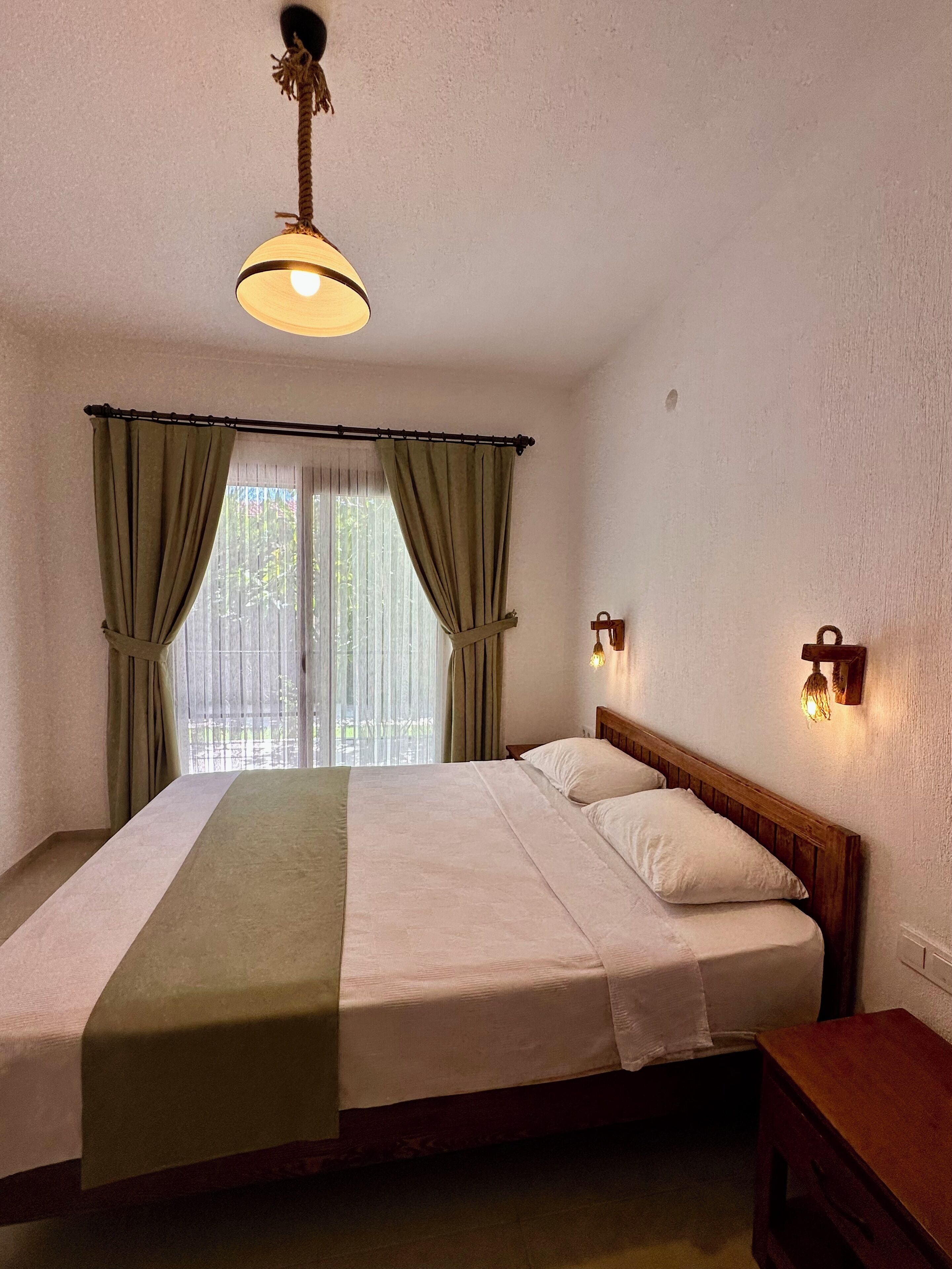 Un dormitorio con cama, cortinas, mesita de noche y lámpara de pared.