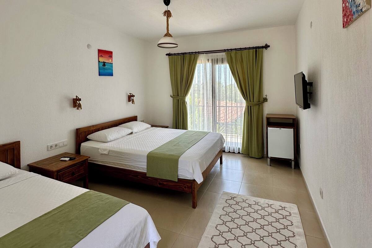 A hotel room with two beds, a small TV, a ceiling fan, and a window with curtains.