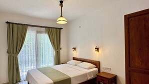 Un dormitorio con cama, una mesita de noche, una puerta de madera y una ventana con cortinas.