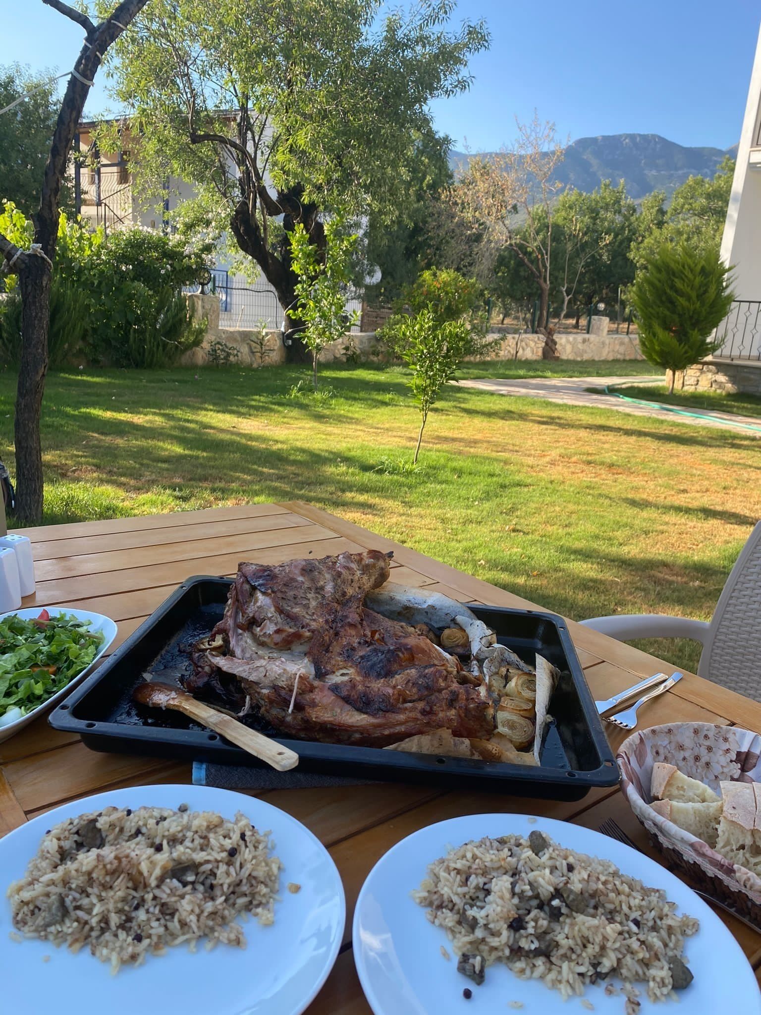 Una mesa de comedor con un cordero asado, dos platos de arroz y una cesta de pan.