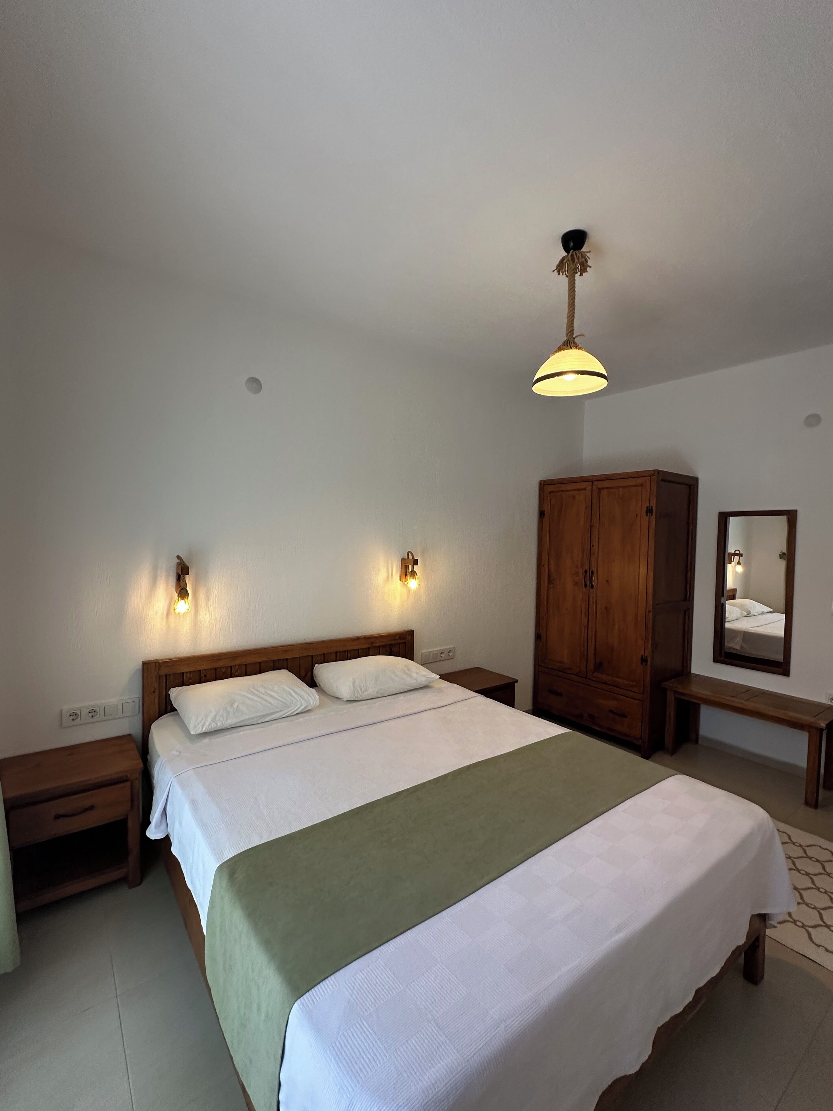Une chambre à coucher avec un grand lit, une armoire en bois, des tables de chevet et un luminaire suspendu.
