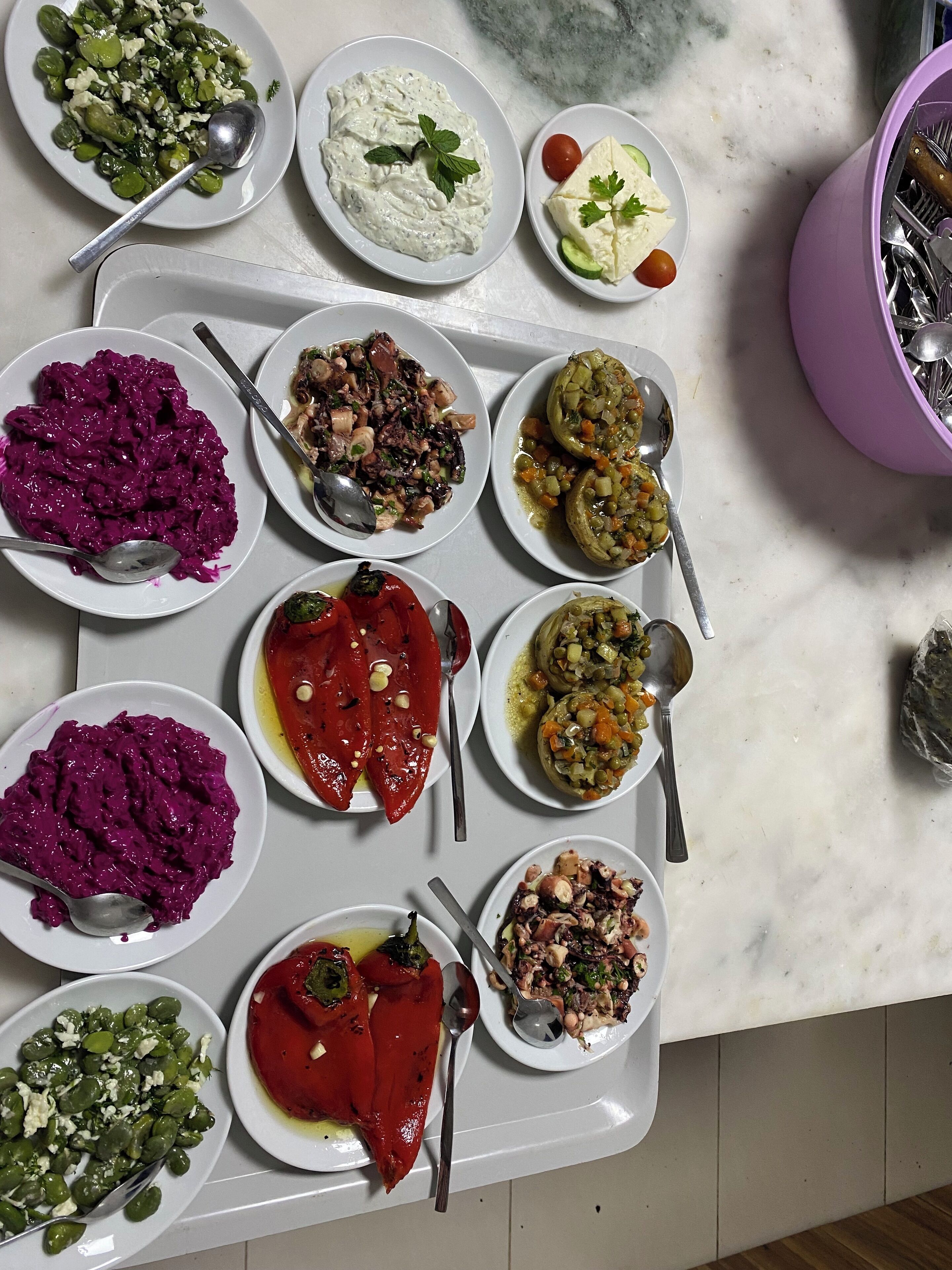 A variety of dishes on a marble countertop, including green beans with cheese, a white creamy dish, a plate with a tomato and cucumber salad, and several other dishes with different ingredients.