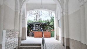 Un couloir au sol en pierre, aux murs blancs et doté d’une rambarde en métal.