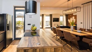 A modern kitchen with a central island, stainless steel appliances, and a dining area with a wooden table and chairs. - Villa Summer Dream - luxury and adventure by MyWaycation (Vrana)