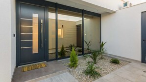 A modern building entrance with a dark door, glass panels, and a small garden area with plants and pebbles. - Villa Summer Dream - luxury and adventure by MyWaycation (Vrana)