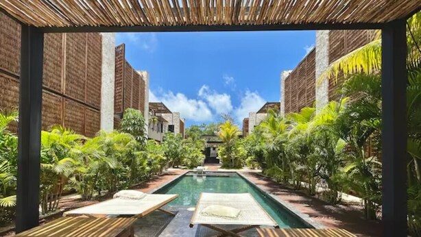 A pool area with lounge chairs and tables, surrounded by lush greenery and traditional architecture. - Bohemian Avant-garde 2BR Apartment (Tulum)