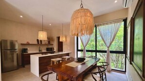 A modern kitchen with a central island, pendant lighting, and a view of greenery through large windows. - Bohemian Avant-garde 2BR Apartment (Tulum)