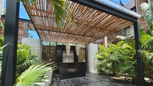 A modern outdoor patio with a bamboo pergola, a black water feature, and lush tropical plants. - Bohemian Avant-garde 2BR Apartment (Tulum)