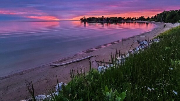 Un lac paisible au coucher du soleil, avec une plage de sable et une végétation luxuriante au premier plan.
