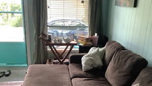 Un salon avec un canapé marron, une petite table sur laquelle se trouve une théière, et une fenêtre avec des rideaux.