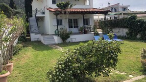 Ein zweistöckiges Haus mit Ziegeldach, einer Veranda und einem kleinen Garten mit Blumentöpfen und Rasen.