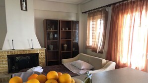 Ein Wohnzimmer mit Kamin, einer Couch, einem Tisch mit einer Orangenschale und einem Bücherregal.