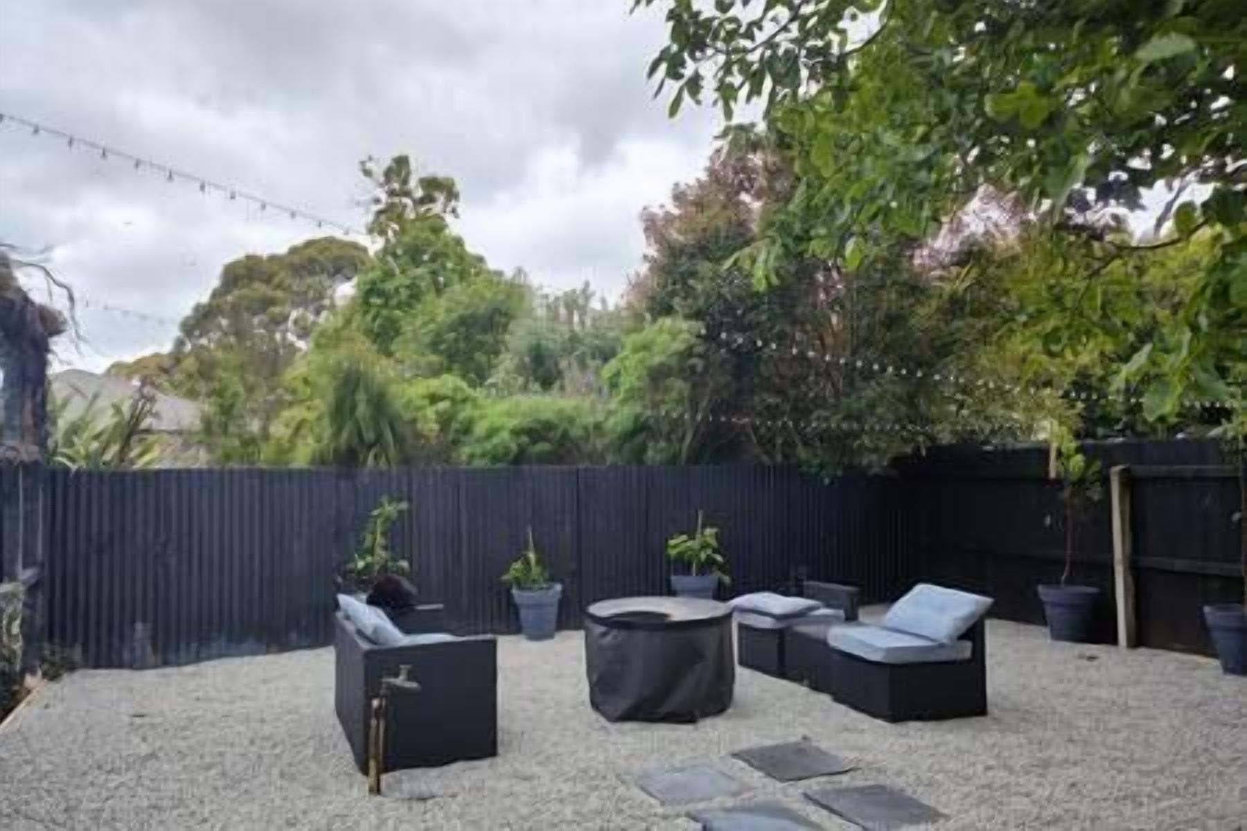 Ein Patio mit Gartenmöbeln, darunter Sofas und einem runden Tisch, umgeben von Kies und einem dunklen Zaun.