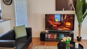 A modern living room with a black leather sofa, a coffee table with a vase of flowers, a bookshelf, and a large painting on the wall.