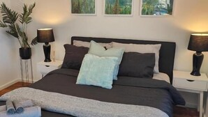 A neatly made bed with a dark headboard, two bedside tables with lamps, and three framed landscape paintings on the wall.