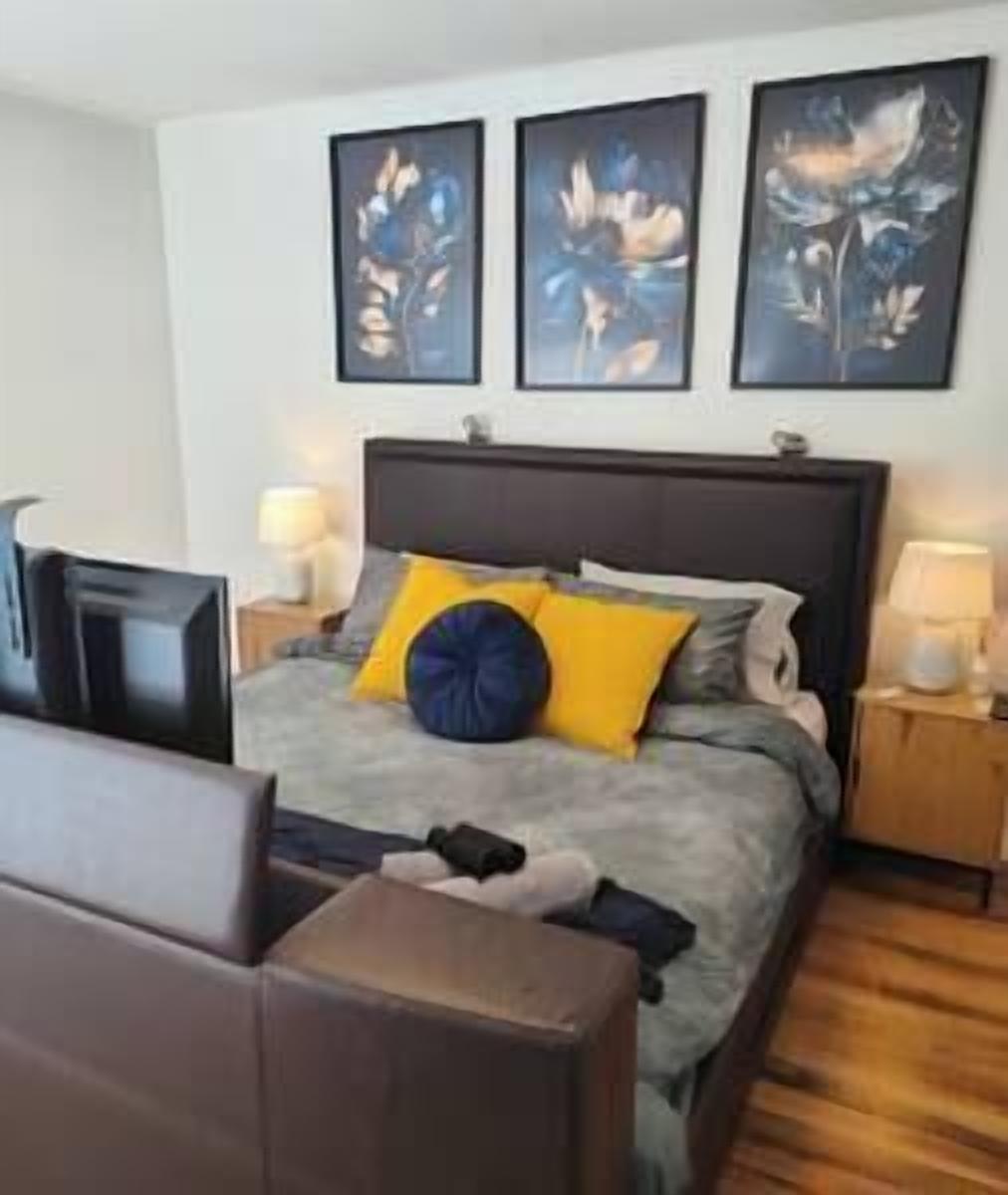 Une chambre d’hôtel avec un lit, une table de chevet, une lampe et trois œuvres d’art encadrées accrochées au mur.
