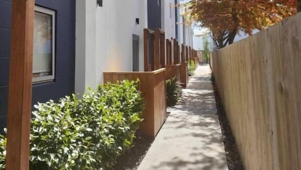 A narrow pathway flanked by buildings with a wooden fence and greenery. - Stylish Townhouse in CBD | 10 Min Walk to One NZ Stadium (Christchurch)